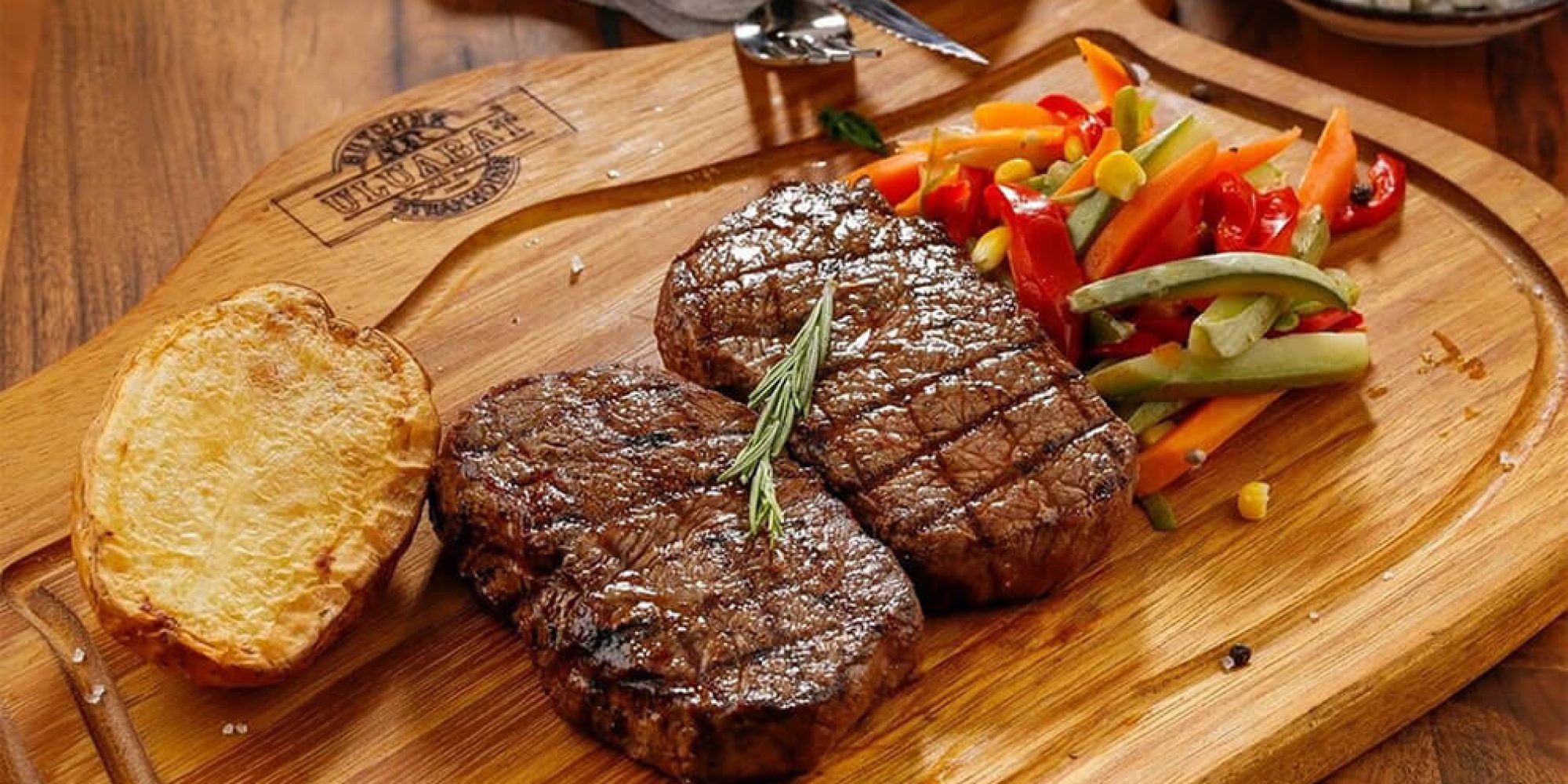 Zwei gegrillte Steaks auf einer Holzplatte angerichtet mit rotem Paprika und Weissbrot.